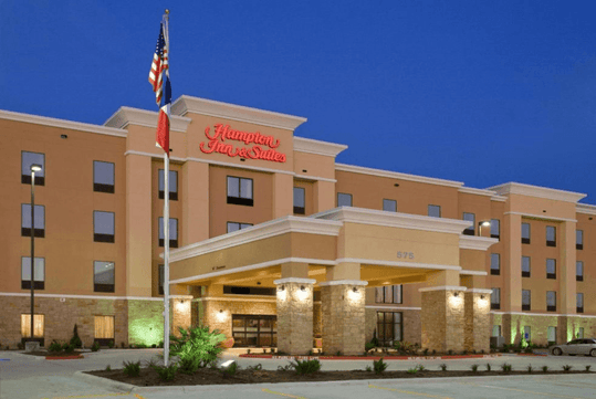 The front of the Hampton Inn & Suites New Braunfels with the exterior lights on at dusk with a clear sky over head.
