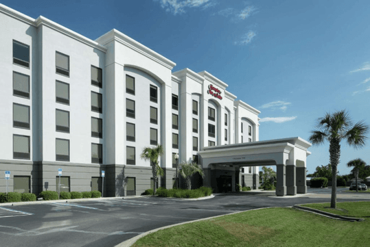 The front exterior and covered entrance of the Hampton Inn & Suites Panama City Beach-Pier Park Area on a sunny day.