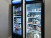 Two black refrigerators with glass doors, one full of drinks, the other full of frozen foods and treats.