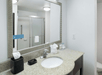 A bathroom with a vanity with a small sink, toiletries, and a large mirror in a hotel room at the Hampton Inn & Suites in Panama City Beach.