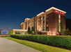 A Hampton Inn & Suites hotel building illuminated at night, with a well-maintained lawn, bushes, and a sign visible near the entrance.