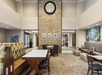 Modern hotel lobby with a high ceiling, stone accent wall, booth and table seating, cushioned benches, and framed artwork on the walls.