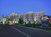 Exterior of Hampton Inn & Suites hotel at dusk, with illuminated signage and landscaped entrance.