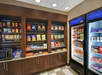 A small convenience store with snacks on shelves, a microwave, a basket, and refrigerated beverages in glass-door coolers.