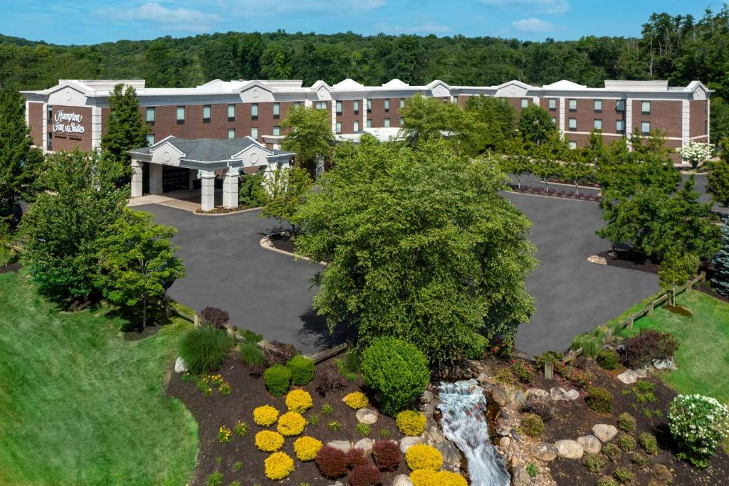 Aerial view of a two-story brick hotel with an entrance sign, surrounded by lush greenery and landscaped gardens with a small waterfall in the foreground.