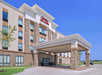Front view of a Hampton Inn & Suites hotel with a stone and stucco exterior, covered entrance, and signage.