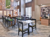 Modern, spacious seating area with high tables, barstools, and chairs in a brightly lit, contemporary setting featuring hanging lights and a decorative wall panel.