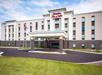 Hampton Inn & Suites building with a modern exterior, featuring a covered entrance, flags, and landscaped surroundings on a clear day.