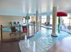 Indoor pool area featuring a wading pool with a red mushroom waterfall, a small jacuzzi, and lounge chairs. A safety fence surrounds part of the pool.