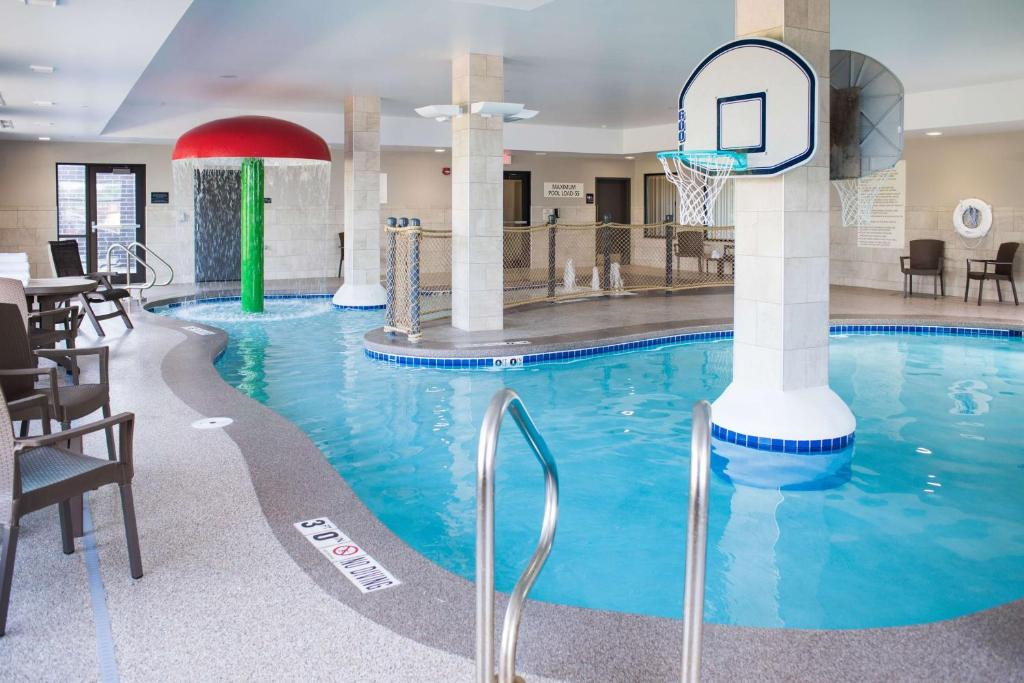 Indoor swimming pool with basketball hoops, mushroom waterfall, and a mini water slide. Poolside chairs and safety equipment visible.