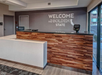 Hotel lobby with a wooden reception desk. A sign on the wall says "Welcome to the Golden State" with a California map outline. A payment terminal is on the counter.
