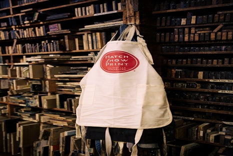 A white apron with a red "Hatch Show Print" logo hangs in front of shelves filled with wooden printing blocks.