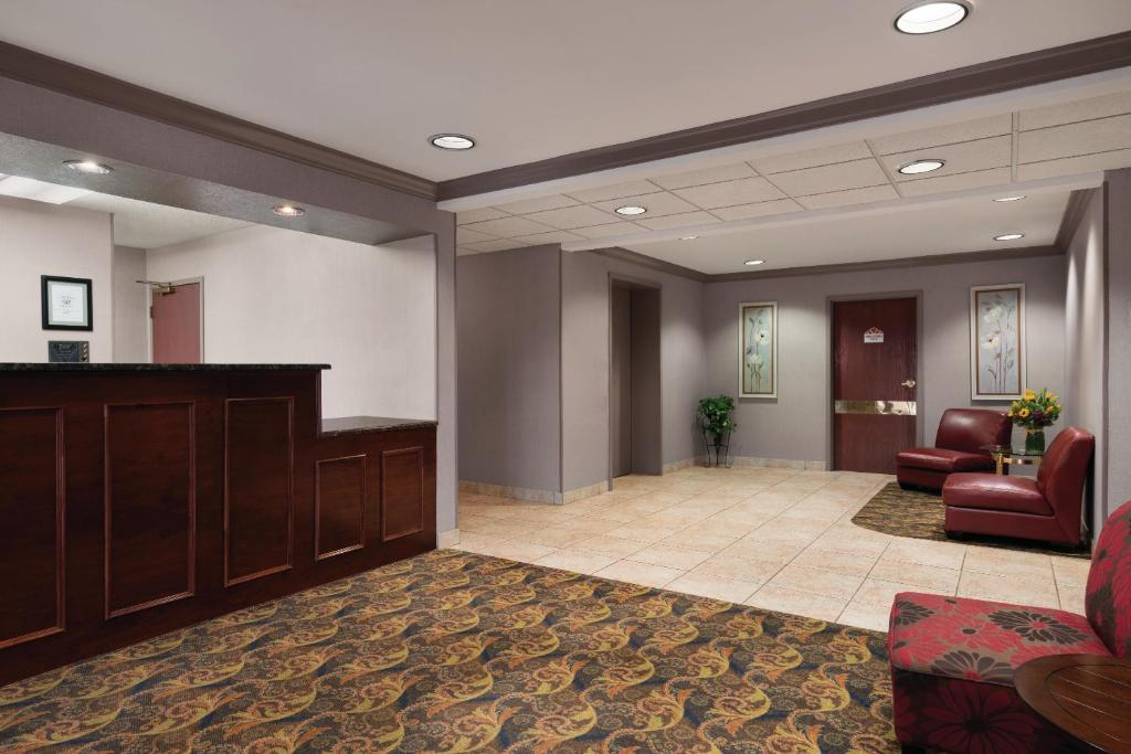 Hotel lobby with a reception desk on the left, patterned carpet, and two red seating areas with floral artwork on the walls.