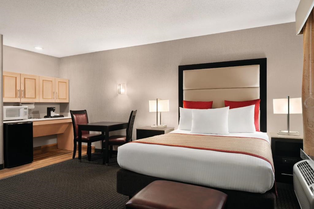Hotel room with a king-sized bed, red and white bedding, a small dining area, a kitchenette with a microwave, and neutral-toned decor.