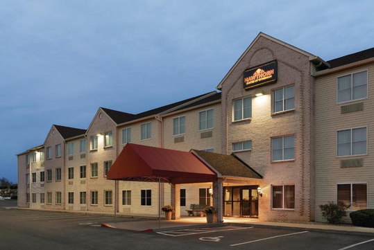 Exterior view of a three-story hotel building with a red awning above the entrance and lit signage on the facade, shown at dusk.