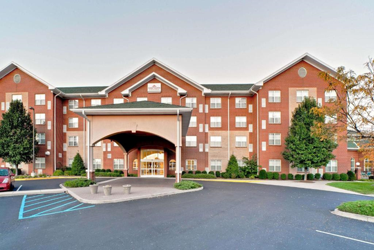 Front view of a multi-story brick building with an arched entrance, ample windows, and surrounding greenery, featuring a blue accessible parking spot in the foreground.