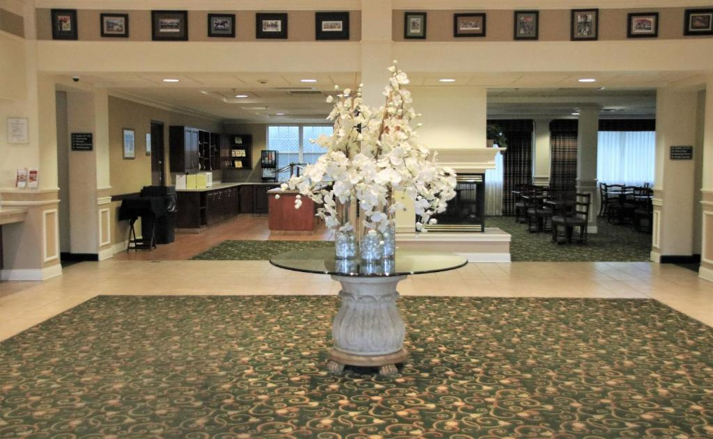 A hotel lobby features a large floral arrangement on a round table in the center, with seating and a fireplace in the background.