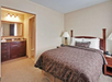 Hotel room with a king-sized bed, bedside lamps, and a view into a bathroom with sink and mirror.