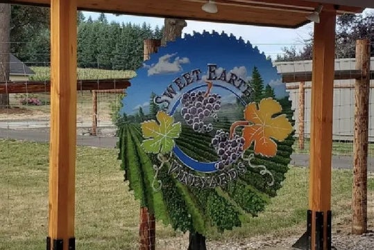 Close up of the colorfully illustrated sign for Sweet Earth Vineyards with flowers and a vineyard painted on it.