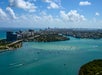 Aerial view of a cityscape with high-rise buildings, turquoise water, boats, and a partly cloudy sky.