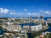 Aerial view of a coastal city with high-rise buildings, waterfront apartments, and canals under a blue sky with scattered clouds.
