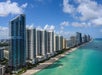 Aerial view of tall beachfront skyscrapers lined along a sandy coast with turquoise water under a partly cloudy sky.