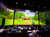 Audience watches a vibrant animated film featuring a train and jungle scenery on a large screen in a theater.