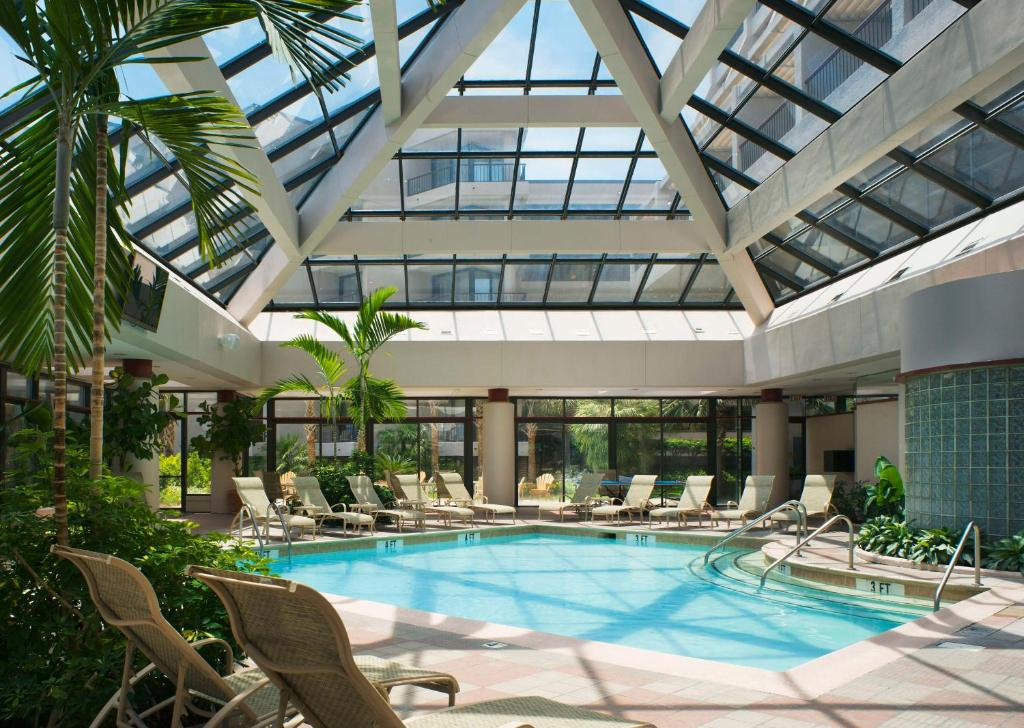 Indoor pool with lounge chairs and tropical plants under a glass ceiling.