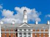 The red brick top levels and gray and white roof of the Hilton Columbus at Easton on a sunny day with clouds in the sky.