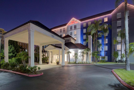 Exterior view of a hotel at night, featuring a lit entrance and surrounding palm trees.