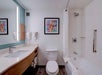 Modern bathroom with a sink, toilet, bathtub, shower, and colorful abstract artwork on the wall. White towels hang by the sink.