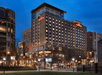 Multi-story Hilton Garden Inn hotel illuminated at night, surrounded by trees and lampposts, with a clear evening sky in the background.
