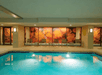 Indoor swimming pool with lounge chairs lined against a wall featuring vibrant tropical-themed artwork.