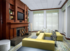 A modern living room with a large wooden fireplace, built-in shelves, a wall-mounted TV, green and patterned seating, and large windows with sheer blinds.