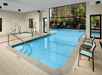 Indoor swimming pool area with two connected pools, pool lifts for accessibility, and chairs alongside. Large windows offer natural light and a view of the outdoor greenery.