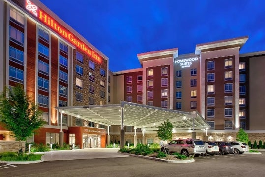 View looking up at the front of the Hilton Garden Inn Columbus Easton with cars parked out front at dusk.
