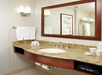 Bathroom with a granite countertop, sink, mirror, and wall-mounted light. Towels and toiletries are on the counter. A hairdryer and toilet paper are stored underneath.