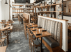 A large dining room with brown tables and chairs and shelves with glassware dividing the room at the Territory Kitchen & Bar.