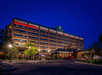 A Hilton Garden Inn hotel building at night, illuminated with exterior lights, surrounded by trees and a parking area in the foreground.