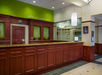 A reception area with a wooden counter, green accent wall, and hanging light fixture. A decorative phrase is displayed above the counter.