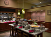 Buffet setup in a restaurant with various dishes and desserts on a granite counter. Overhead lighting and wooden decor are visible. A clock hangs on the wall.