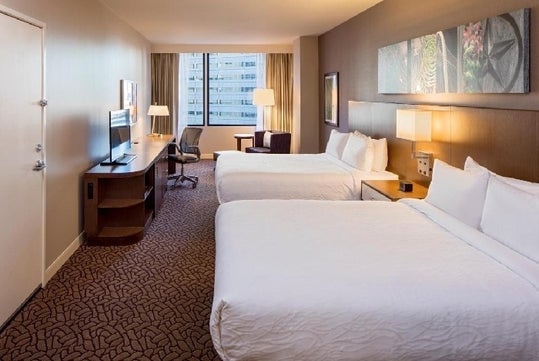 Two queen beds, flat-screen TV, work desk, small sofa and an expanded window with a view.