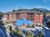 Aerial view of a large hotel with a blue roof, surrounded by roads and trees, with mountains in the background.