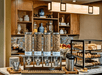 Breakfast bar with cereal dispensers, pastries, and fruits. Wooden cabinetry and shelves with decorative items in the background.
