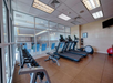 A gym room with treadmills, a rack of dumbbells, an exercise ball, and a view of an indoor pool through glass walls.