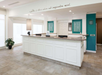 Hotel reception desk with a white counter, teal accents, and a plant. A quote is displayed above.