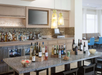A bar area with bottles of wine, liquor, and beer on display. Glasses are stored above a granite countertop. Two yellow pendant lights hang from the ceiling.