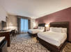 Two queen beds with premium beddings, bedside lamps, desk, and TV in a guest room.