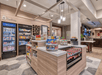 A modern hotel convenience shop with shelves of snacks, drinks in coolers, and various packaged goods on display under bright lighting.