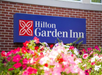 Sign for Hilton Garden Inn on a brick wall, surrounded by vibrant flowers in the foreground.